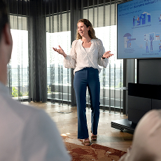 Vrouw die een presentatie geeft aan collega's in een moderne vergaderruimte met grote ramen.
