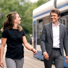 Twee mensen lopend en lachend samen bij een tramhalte buiten.