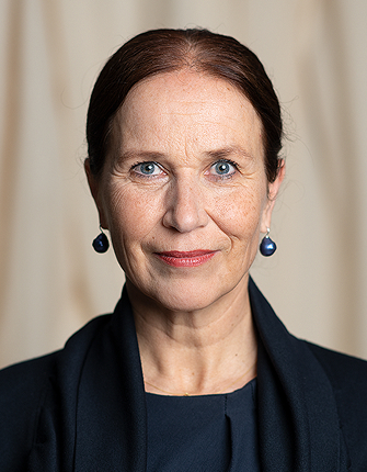 Vrouw met donker haar, blauwe ogen en donkere oorbellen, neutrale achtergrond.