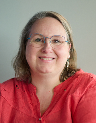 Lachende vrouw met bril en rood shirt, grijze achtergrond.