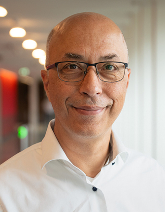 Lachende kale man met bril en wit overhemd, kantoorachtergrond.