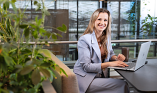 Persoon werkt op een laptop aan een tafel in een groene, open kantooromgeving.