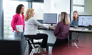 Personen werken samen in een kantoorruimte met meerdere computerschermen.