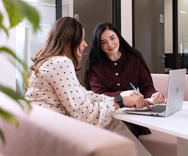 Twee personen zitten samen aan een tafel en werken aan een laptop in een kantoorruimte.