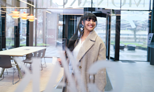 Persoon staat in een moderne entreehal met glazen wanden en uitzicht op buiten.