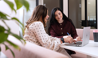 Twee personen zitten samen aan een tafel en werken aan een laptop in een kantoorruimte.