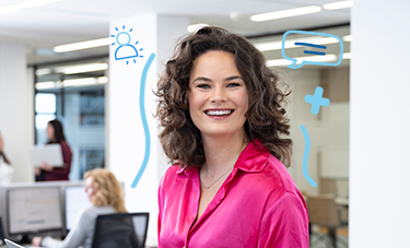 Persoon werkt aan een bureau in een open kantoorruimte met collega’s op de achtergrond.