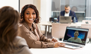 Personen in een kantoorruimte tijdens een videogesprek op een laptop.