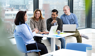 Een groep personen overlegt aan een tafel in een kantoorruimte met uitzicht naar buiten.