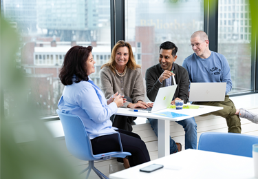 Een groep personen overlegt aan een tafel in een kantoorruimte met uitzicht naar buiten.