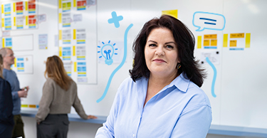 Persoon staat bij een laptop voor een wand vol scrumborden waar anderen overleggen.