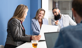 Personen zitten samen aan een tafel in een vergaderruimte en bespreken iets op een laptop.
