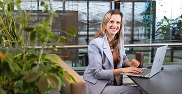 Persoon werkt op een laptop aan een tafel in een groene, open kantooromgeving.