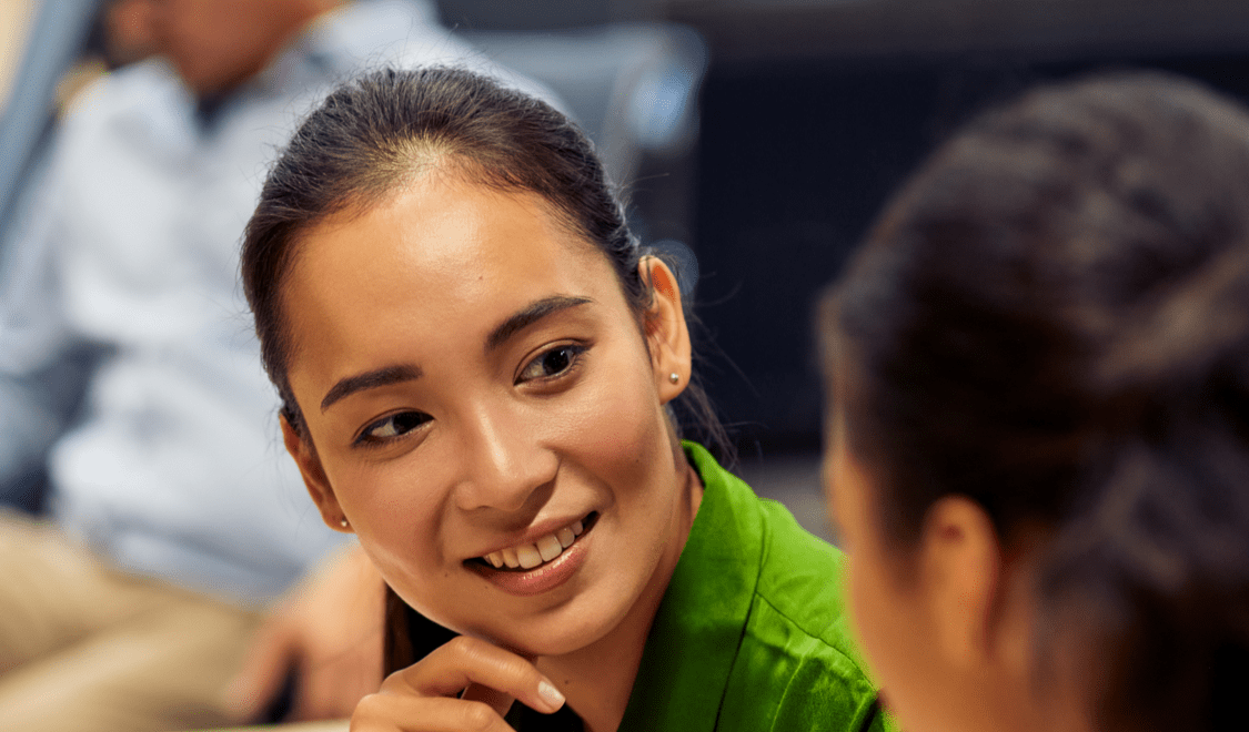 Woman in green blouse talking to colleague with her back turned to camera