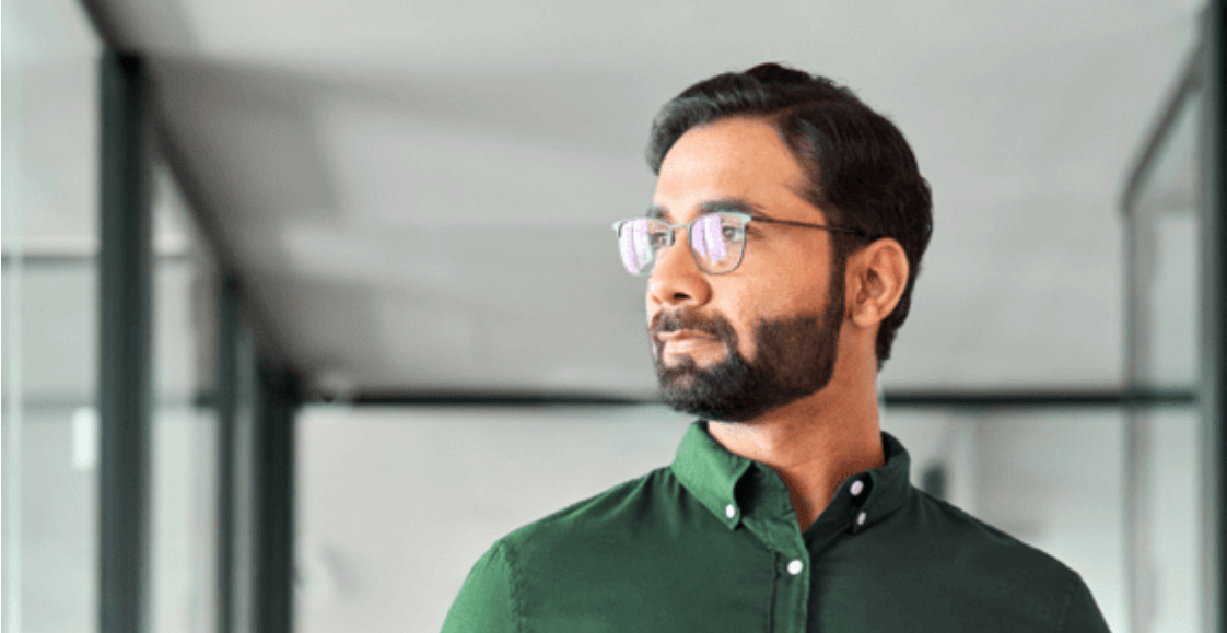 Man with glasses in green shirt holding tablet within an office setting