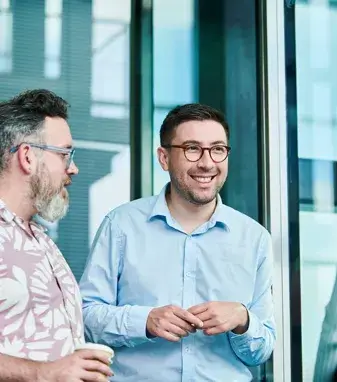 Man in floral shirt talking to male colleague in blue shirt