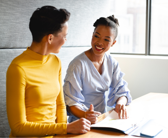 Two colleagues engaged in conversation while seated in an office environment.