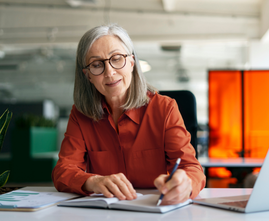 A professional sat in an office writing in a notebook.