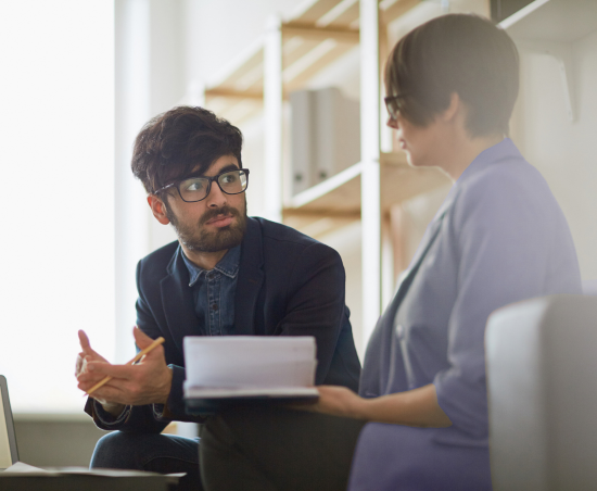 Two colleagues engaged in conversation while seated in an office environment.