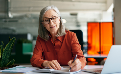 A professional sat in an office writing in a notebook.