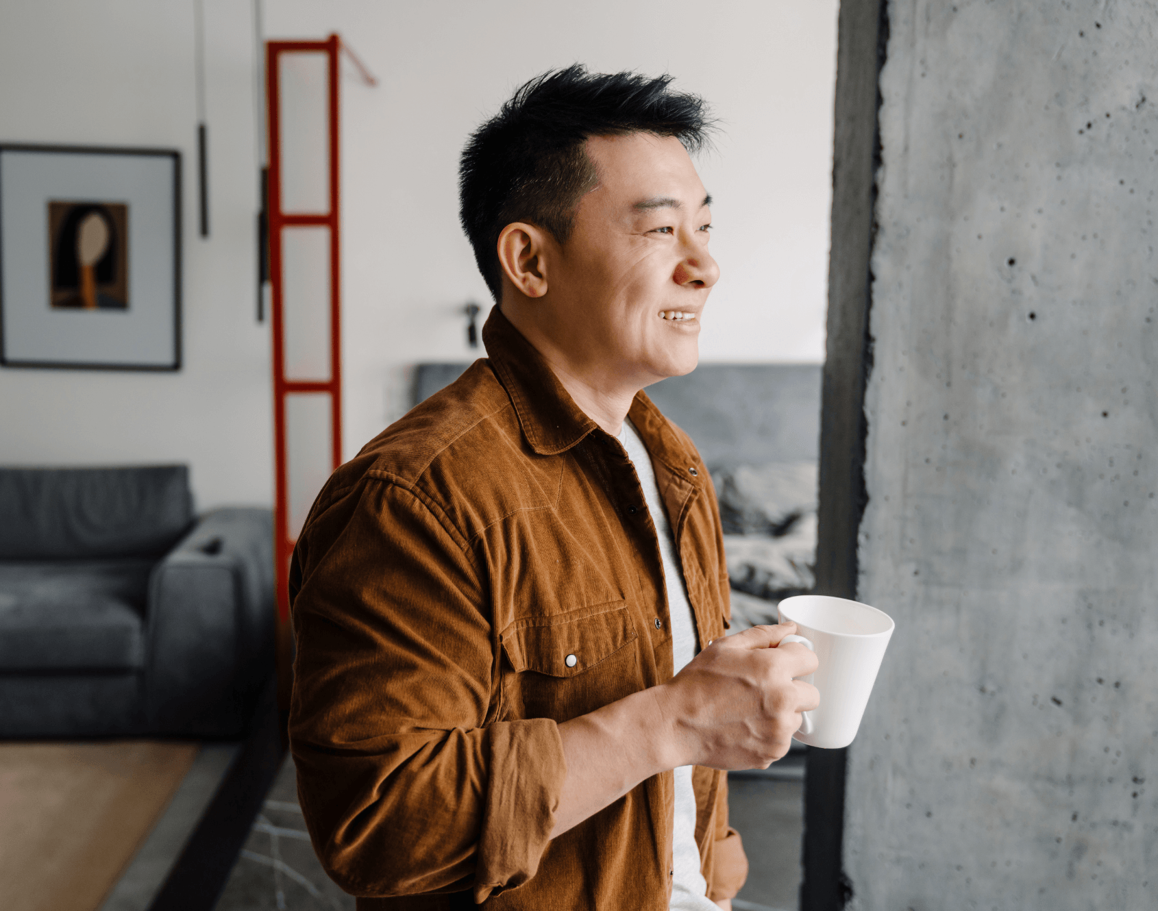 A professional standing in an office space, holding a cup and looking out of a window.