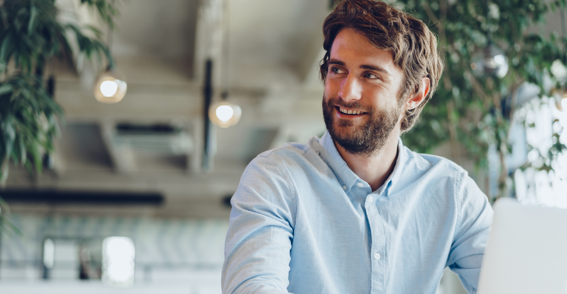 A professional smiling while seated at a work desk.