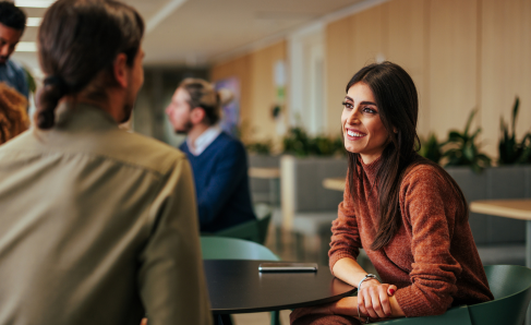 Two colleagues engaged in conversation while seated in an office environment.