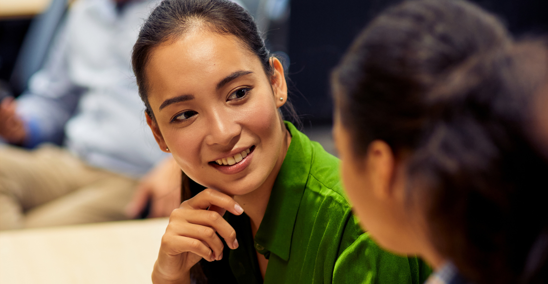 Two colleagues engaged in conversation while seated in an office environment.