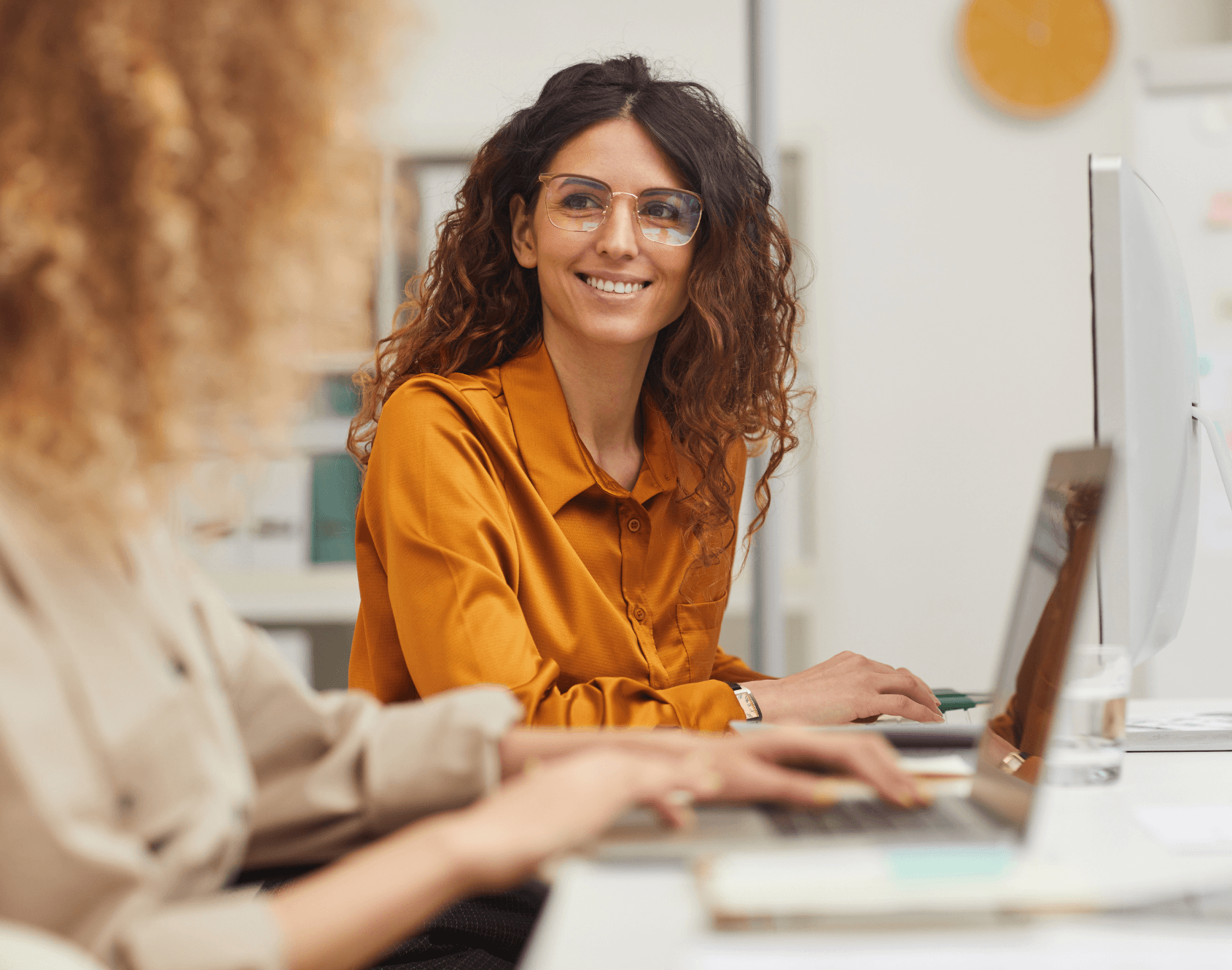 Two colleagues engaged in conversation while seated in an office environment.