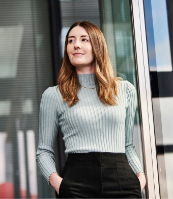 A professional smiling while stood in an office environment.
