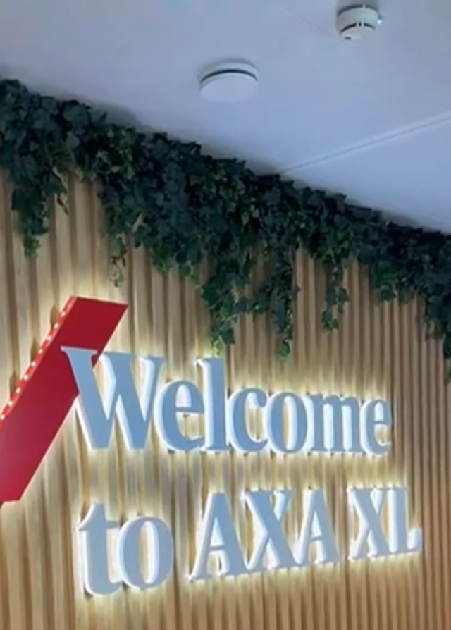 Panneau lumineux « Bienvenue chez AXA XL » sur mur végétalisé.