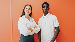 Deux personnes en tenue claire devant un mur orange.