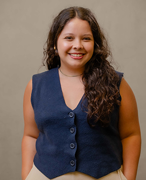 Person with curly hair wearing vest smiling