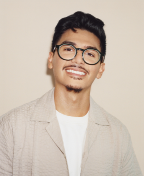 Person with glasses smiling against plain background