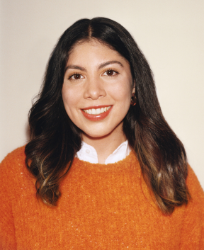 Person in orange sweater smiling against plain background