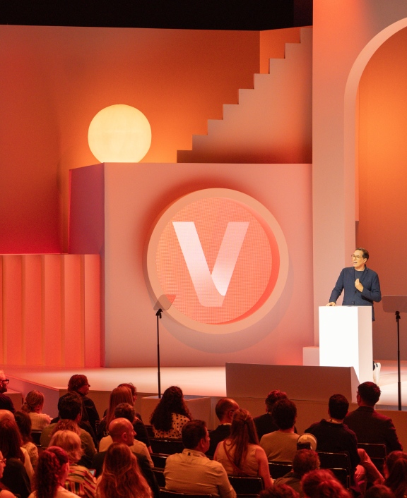 Speaker presenting on orange stage before audience