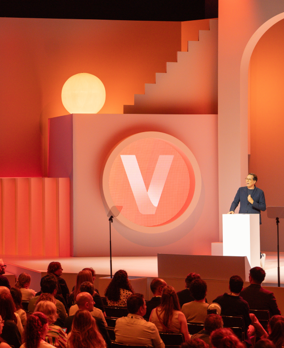 Speaker presenting on orange stage before audience