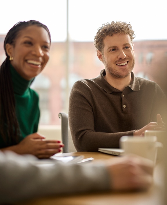 Two coworkers smiling and talking at table indoors