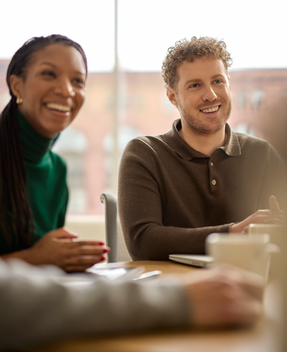 Two coworkers smiling and talking at table indoors