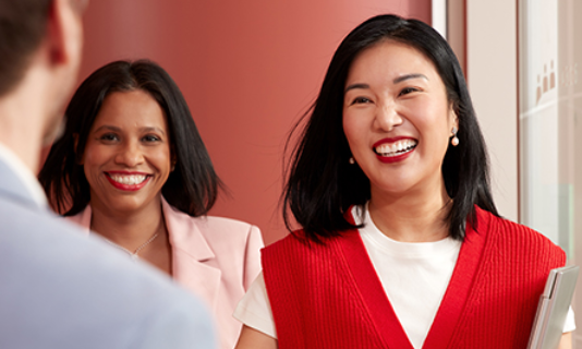 Two people greeting colleague, one holding tablet in office