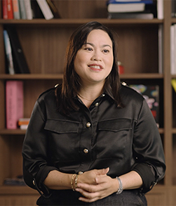 Person seated indoors in front of bookshelf background, speaking on camera
