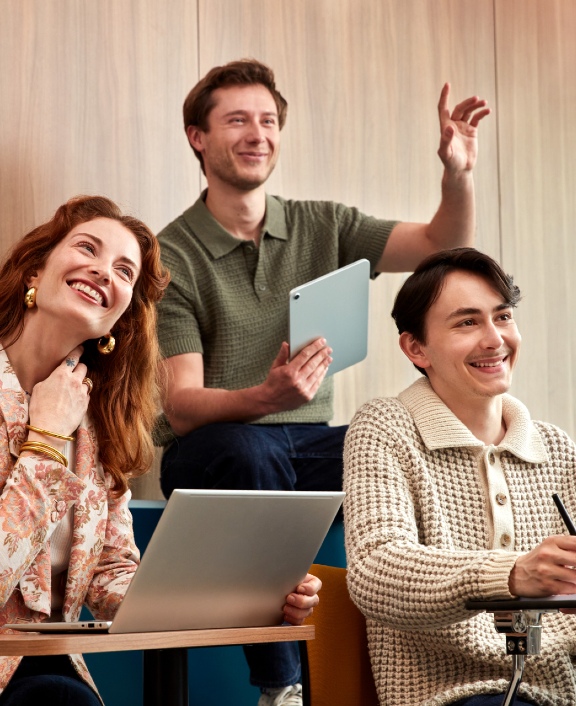 Three people in a classroom using laptops, tablet