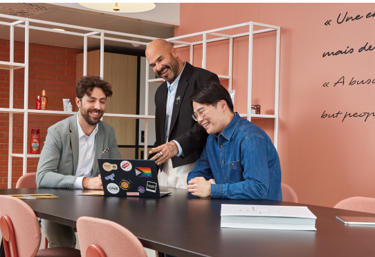 Three coworkers collaborating at table with laptops in office