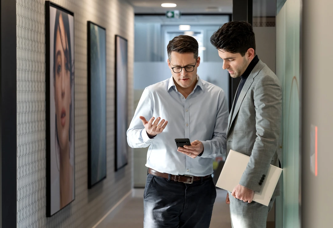 Two colleagues reviewing phone in office hallway