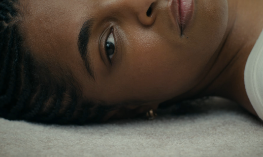 Close-up of a woman lying on a carpet, gazing at the camera.