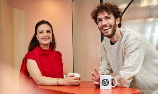 Deux personnes souriant et discutant avec des tasses de café.