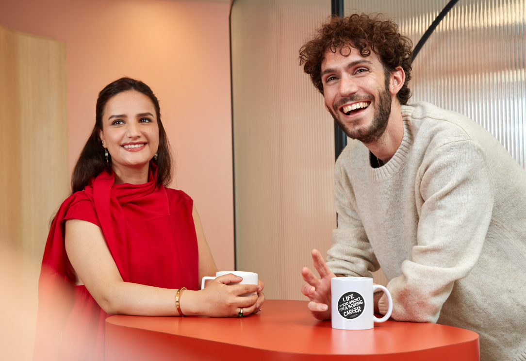 Two people smiling and talking with coffee mugs