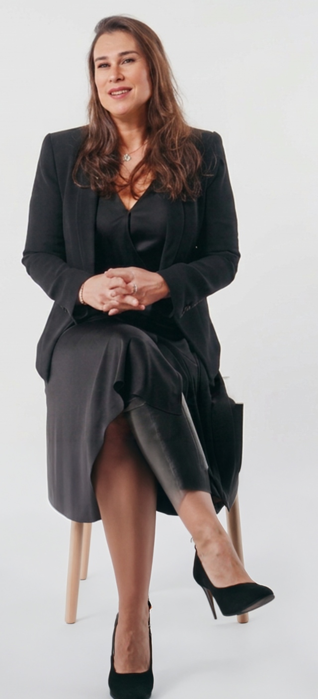 A Women standing in black outfit on plain backdrop