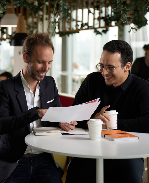 Two people reviewing document together at café table with coffee