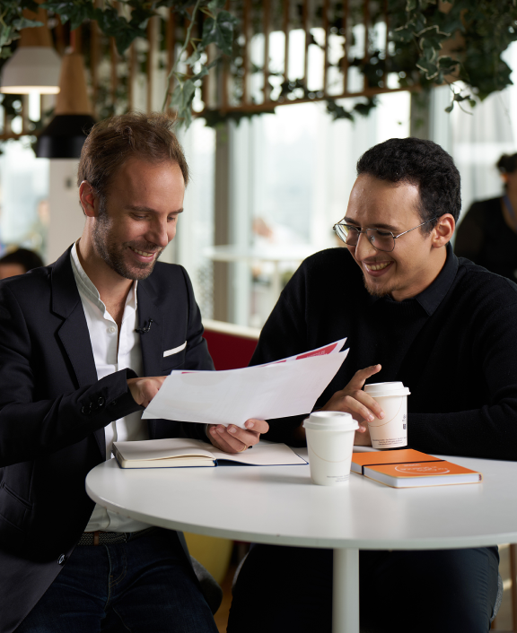 Two people reviewing document together at café table with coffee